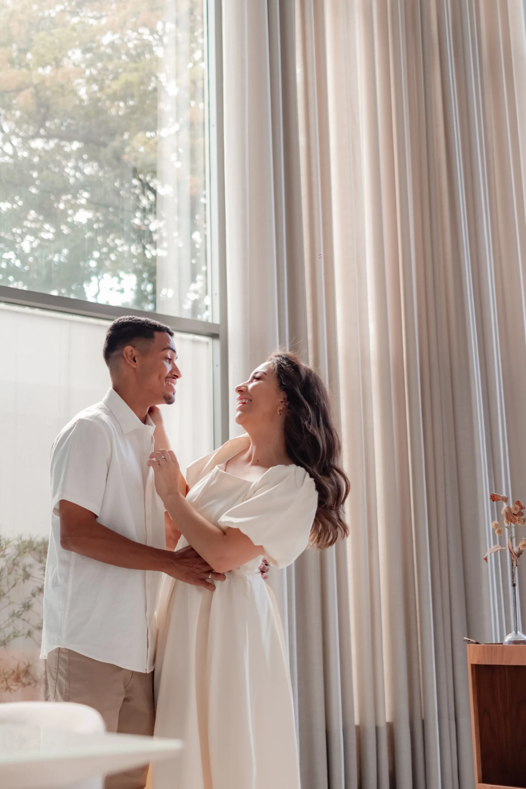 A happy couple sharing a candid, romantic moment together in a brightly lit modern living room or event space.