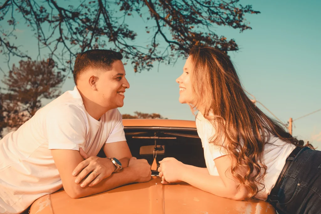 A smiling couple leaning against the hood of a car