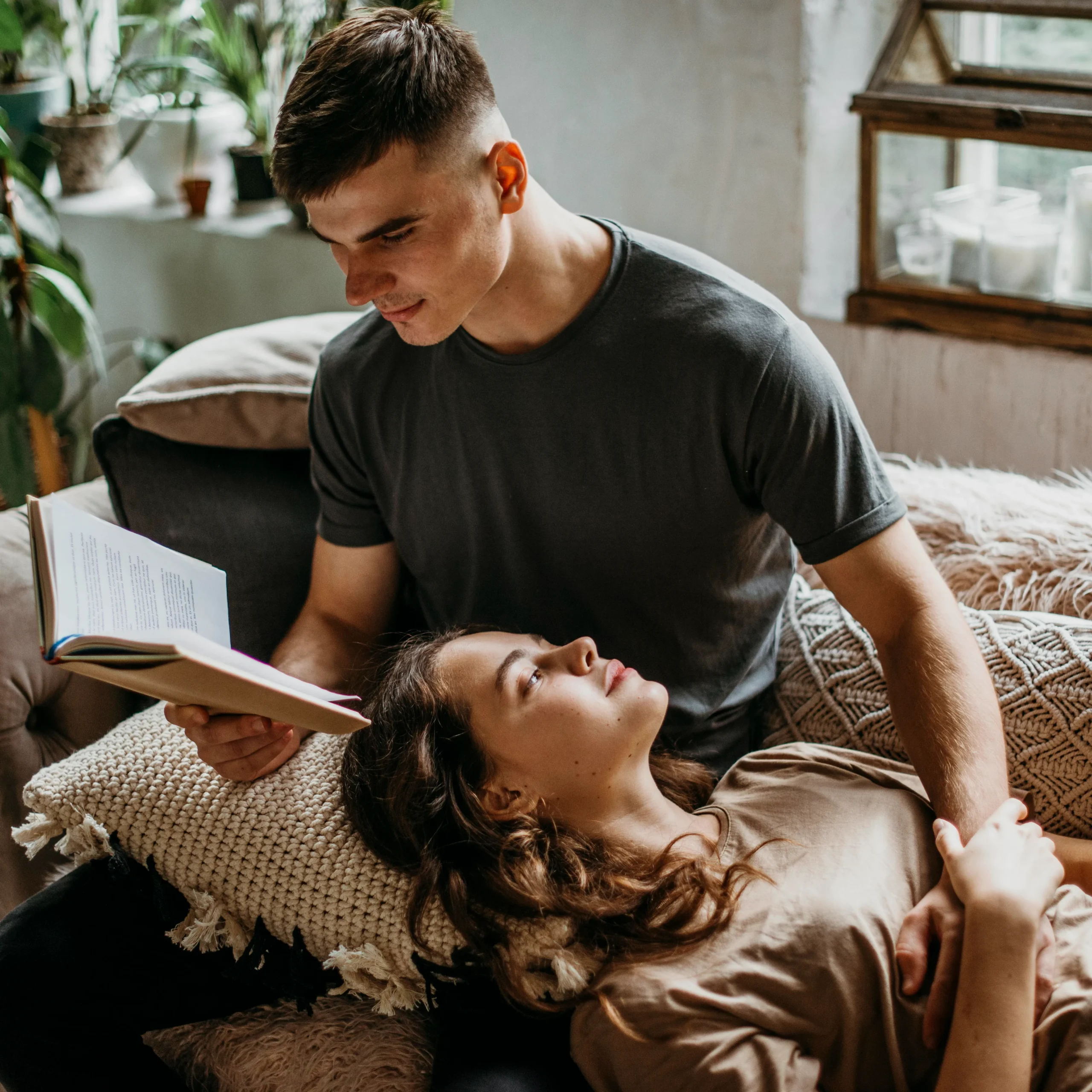 A man reading an open book to a woman resting her head on his lap.