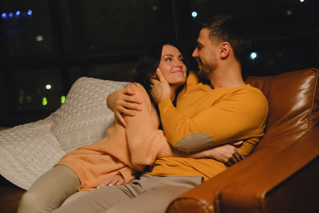 A man and woman in sweaters cuddling together on a leather chair.