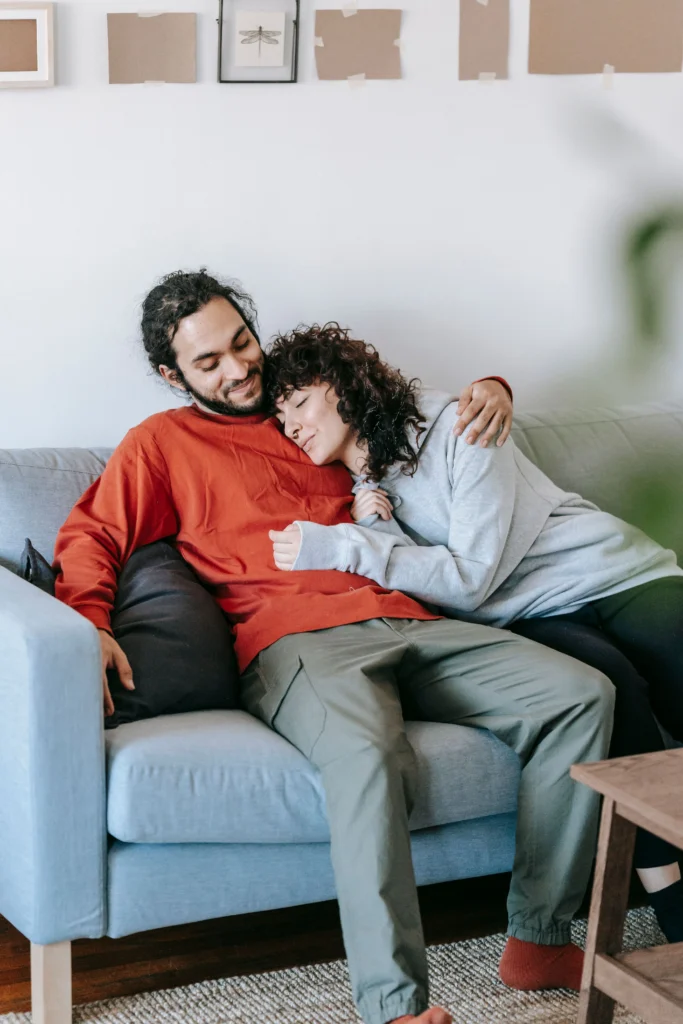 A man and a woman cuddling on a grey couch.