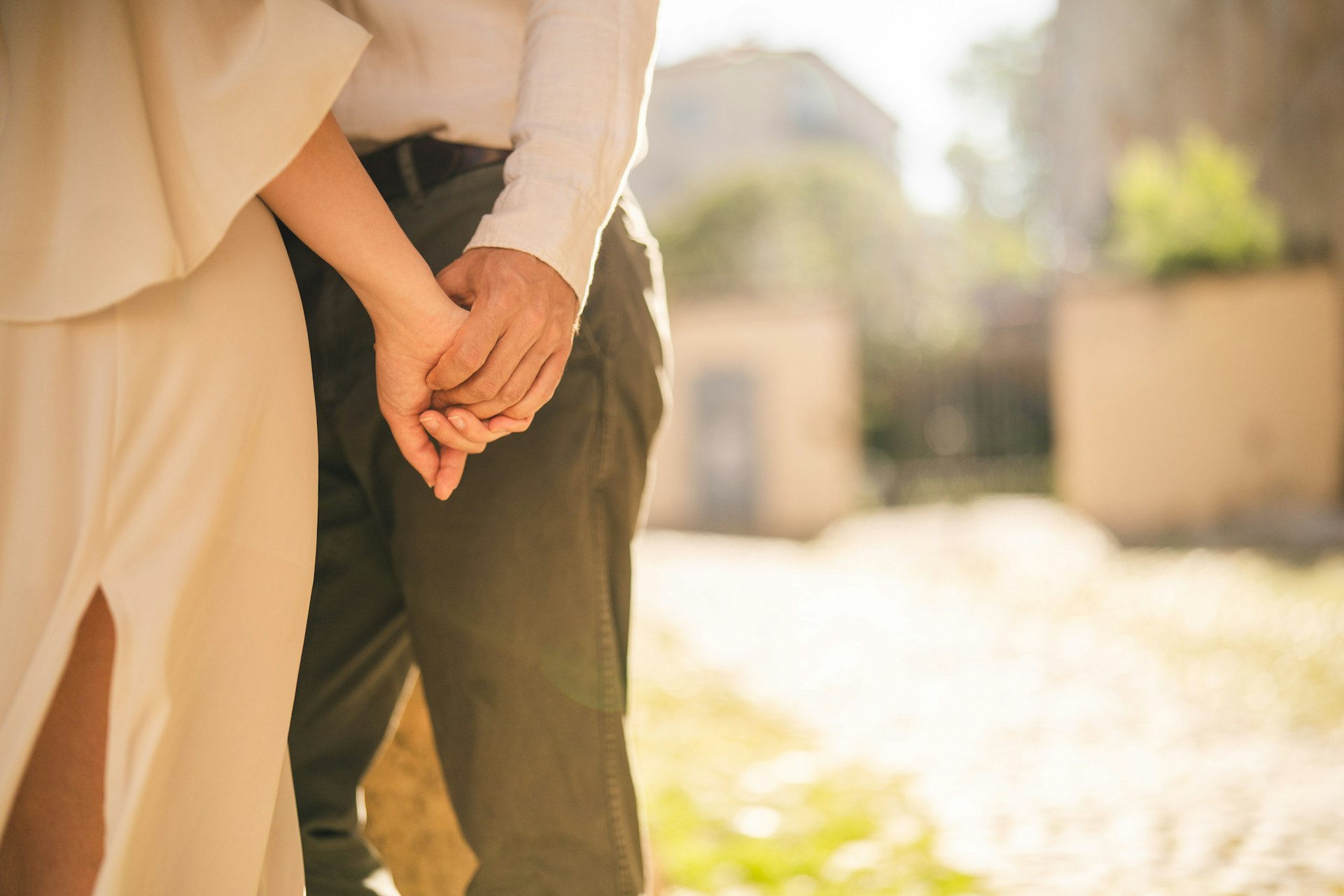 A close-up of a couple holding hands during golden hour with warm sunlight glowing behind them
