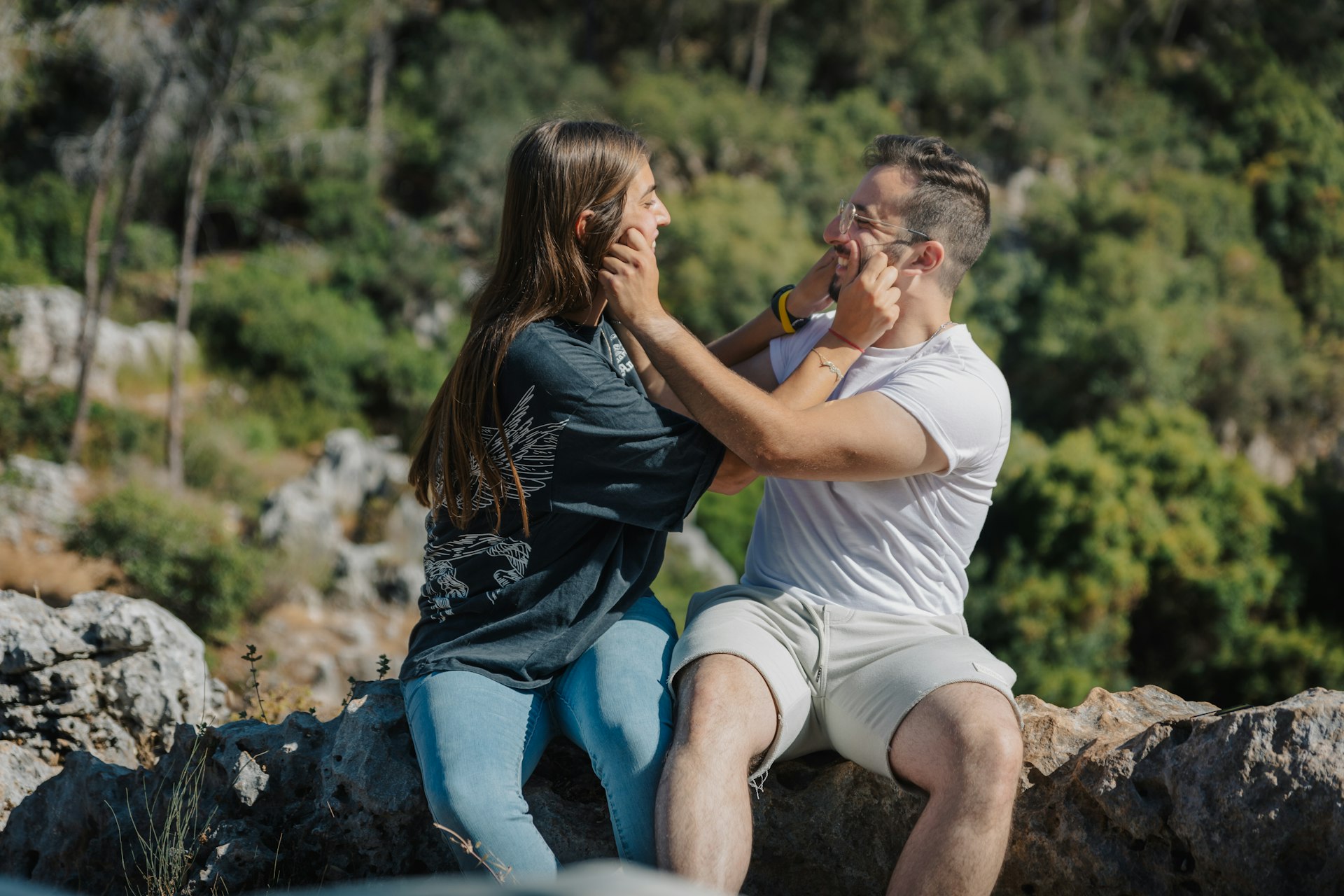 A smiling couple playfully touching each other's faces outdoors